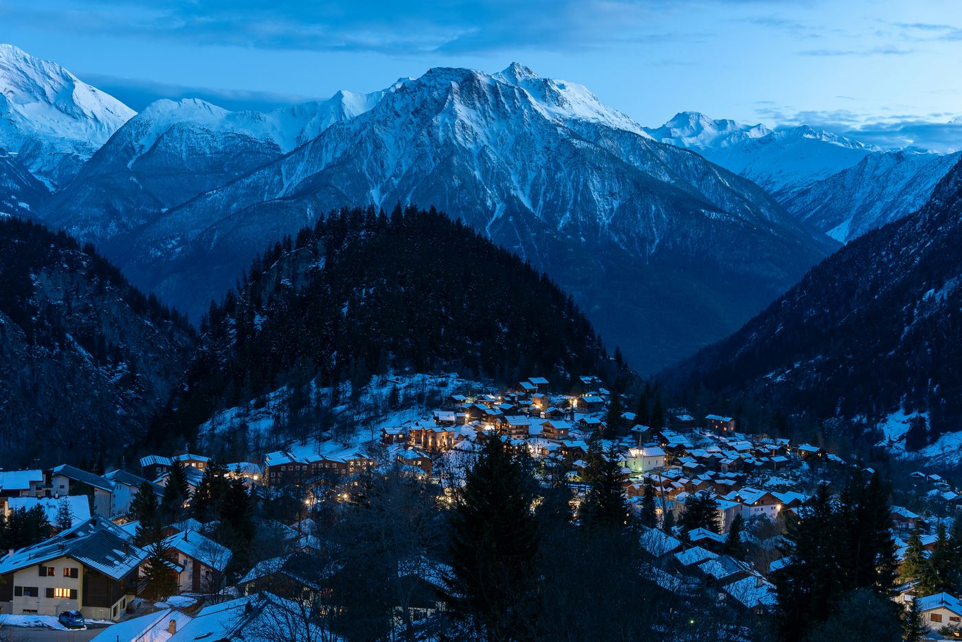 Un village valaisan à l'heure bleue, ses lumières allumées au crépuscule.